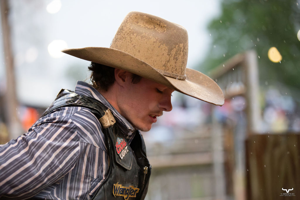 Bull rider in dust-covered cowboy hat, head down before the ride